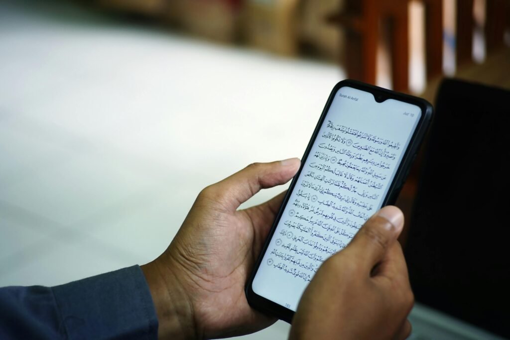 pexels-photo-11244640-11244640 A man reading the Quran on a smartphone inside a mosque, symbolizing modern technology meeting traditional faith.